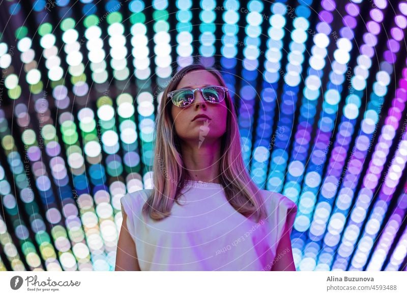 Teenager-Hipster-Mädchen in stilvollen Brillen stehen auf blauen Tunnel mit Neonlicht Wand Hintergrund, weibliche Teenager Mode-Modell hübsche junge Frau Blick auf Nachtclub Stadt Licht glühen