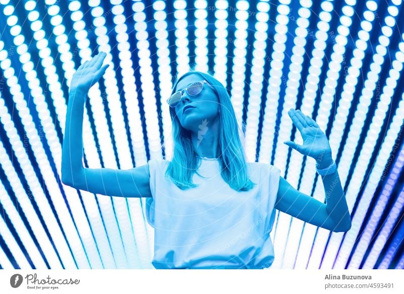 Teenager-Hipster-Mädchen in stilvollen Brillen stehen auf blauen Tunnel mit Neonlicht Wand Hintergrund, weibliche Teenager Mode-Modell hübsche junge Frau Blick auf Nachtclub Stadt Licht glühen