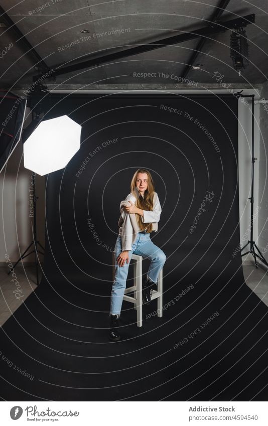 Fröhliche Frau sitzt auf einem Stuhl im Fotostudio Model Lächeln positiv Stil Optimist trendy Vorschein octabox Glück lange Haare heiter hölzern sitzen