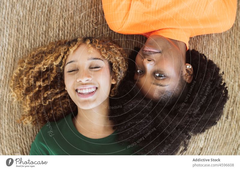 Positive multiethnische Freundinnen, die zusammen auf einem Teppich liegen Frauen Stock Zusammensein Lügen Lächeln Glück Freundschaft sich[Akk] entspannen