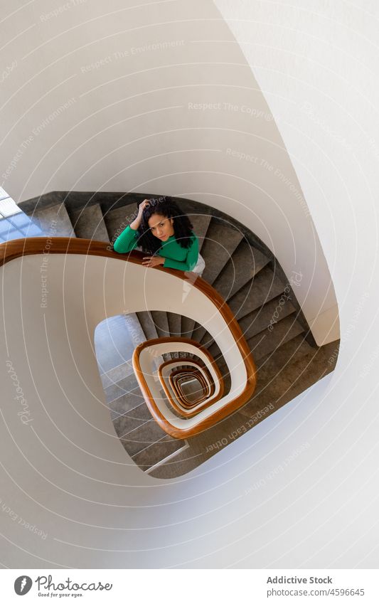 Schwarze Frau auf Wendeltreppe stehend Gebäude Treppenhaus Spirale Reling modern Stil wohnbedingt Afroamerikaner schwarz dunkles Haar brünett feminin Dame Haus