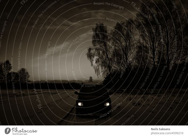 schwarzes Auto mit Scheinwerfern auf schneebedeckter glatter Waldstraße in Lettland Landschaft. Monochrom sepia. Automobil Hintergrund schön Schneesturm blau