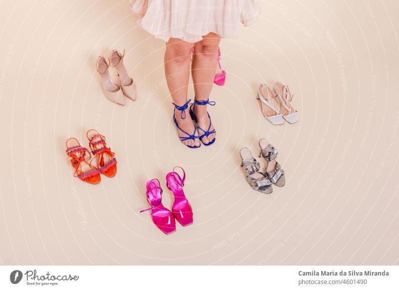 Stilvolles Mädchen im rosa Plissee-Kleid, umgeben von verschiedenen Schuhen. Sie ist in einem rosa Faltenrock gekleidet, an ihren Füßen blaue Schuhe. Sortiment