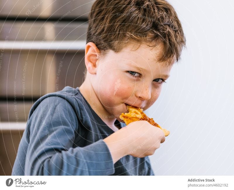 Fröhlicher Junge isst Pizza in der Küche essen Kind Küchengeräte heimisch zu Hause Lebensmittel Mahlzeit Spielfigur hungrig Vergnügen genießen Gebäck lecker