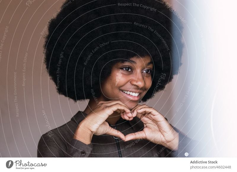 Lächelnde schwarze Frau zeigt Herzgesten durch Ringlampe Blogger gestikulieren Liebe Vlogger Freizeit Afro-Look Frisur feminin Vorschein Glück charmant brünett