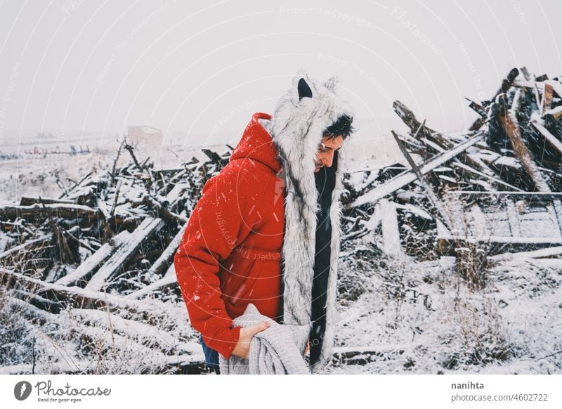 Junger Mann mit Pelzmütze und rotem Kapuzenpulli genießt einen verschneiten Tag Winter Schnee Spaß lustig genießen kalt frieren gefroren Leben Lifestyle weiß