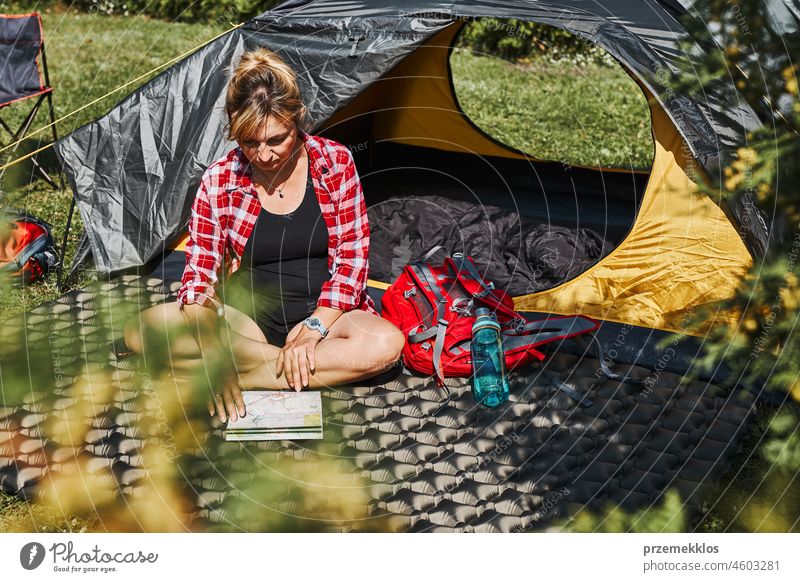 Frau plant nächste Reise, während sie mit Karte im Zelt sitzt. Frau entspannt im Zelt beim Camping im Sommerurlaub Urlaub Ausflug Abenteuer Campingplatz reisend