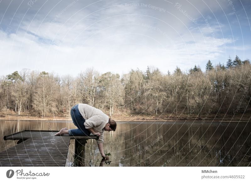 Frau am Steg am Kratersee mit Pflanze in der Hand See Ufer Maar Teich Holzsteg Urlaub Winter kahl kalt Wasser Glücksklee Pflanzen Ruhe Einsamkeit Entspannung