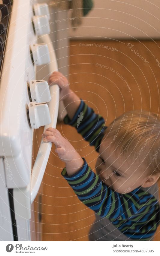 Ein 18 Monate altes Kind hängt sich an den Griff der Backofentür; die gefährliche Aktivität führt dazu, dass das Haus babysicher gemacht wird Baby Hand Säugling