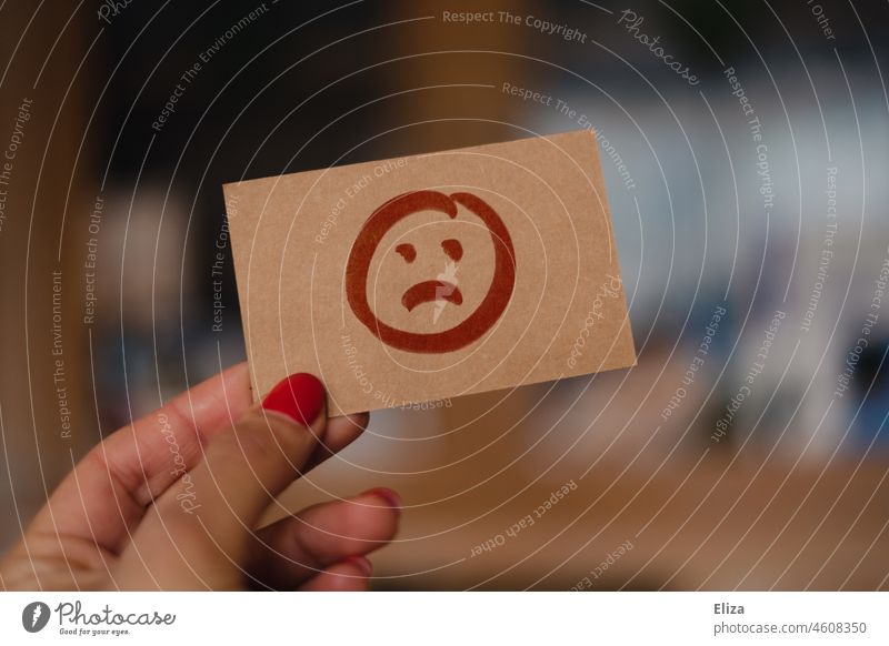 Weibliche Hand hält ein Schild mit traurigen Smiley Traurig Emotionen unzufrieden unglücklich Frau Bewertung Frust Burn Out Depression Problematik Zettel