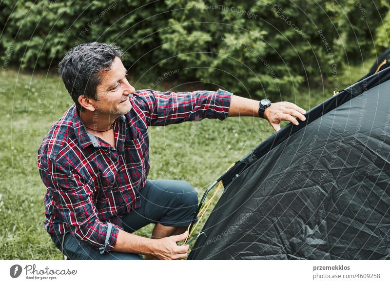 Mann, der ein Zelt auf dem Campingplatz während der Sommerferien aufbaut. Vorbereiten des Campingplatzes zum Ausruhen und Entspannen. Urlaub im Freien in der Nähe der Natur verbringen