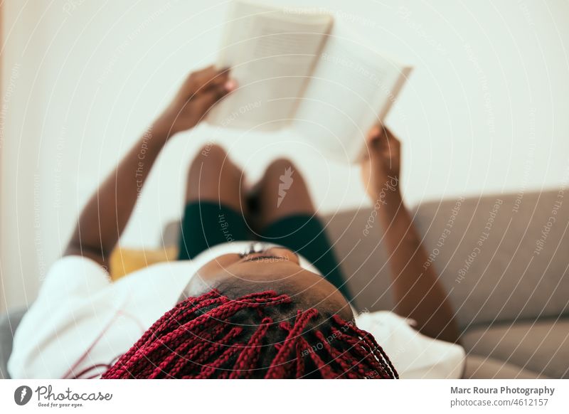 Schwarze Frau liegt auf dem Sofa und liest ein Buch mit den Füßen an der Wand Erwachsener Afrikanisch attraktiv Hintergrund schön Schönheit schwarze Frau heiter