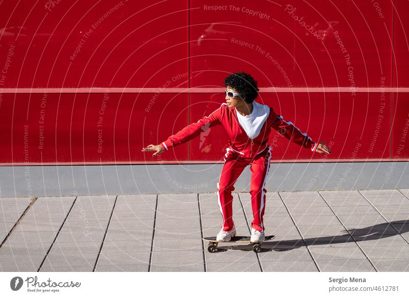 Afroamerikanische Frau mit kurzen Haaren und roter Sportkleidung fährt auf ihrem Skateboard mit rotem Hintergrund Afroamerikaner Spanien Granada Sportbekleidung