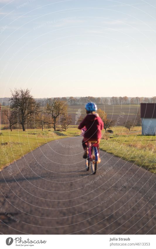 schnell wie der wind,  mit dem Rad fährt sie vorbei Fahrradfahren Kinderrad Radfahrerin Helm feldweg geteert Bäume Obstbäume Obstbaum Ackerland Ackerboden Erde