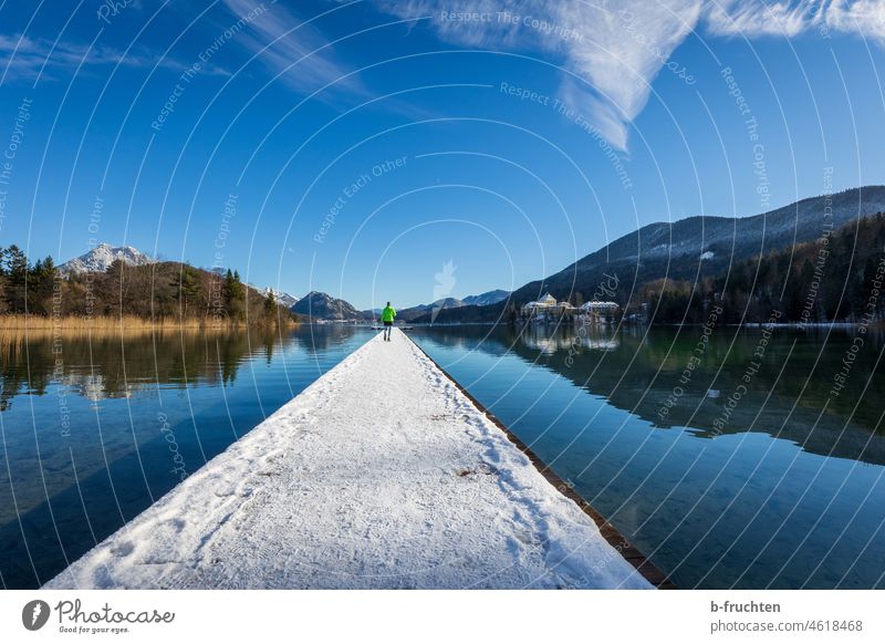 Eine Person steht auf einem langen, schneebedeckten Steg. Winterlandschaft Holzsteg Frau See Landschaft Wasser Natur Seeufer Idylle ruhig Reflexion & Spiegelung