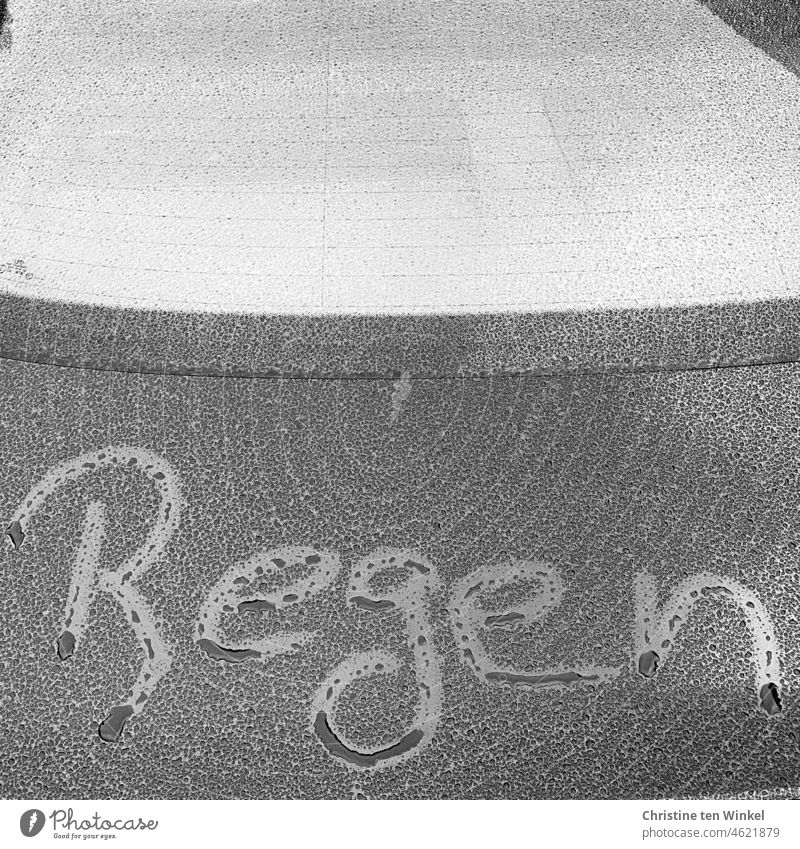 Und immer noch Regenwetter. Das Wort "Regen" wurde mit einem Finger auf ein nasses Auto geschrieben Buchstaben Regentropfen schreiben Wassertropfen