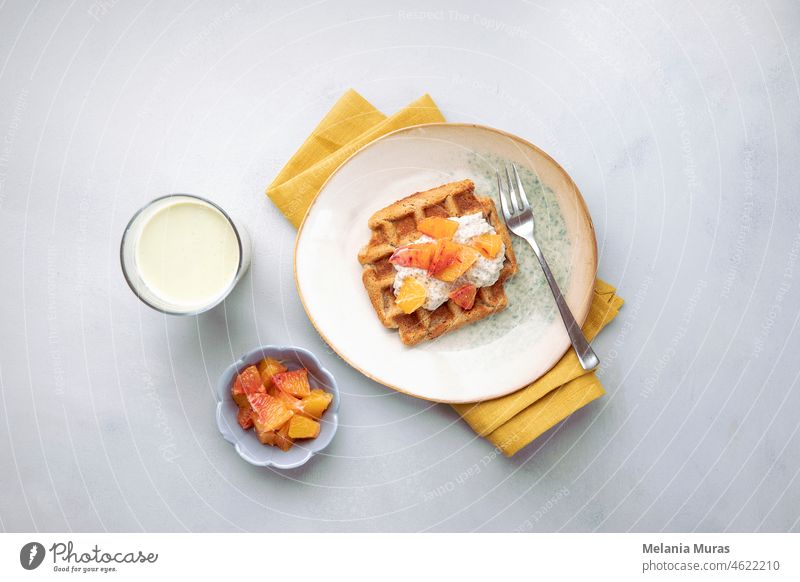 Vegane, glutenfreie Waffeln mit Pudding, Orangen und grüner Milch auf blauem, neutralem Hintergrund. Gesunde Mahlzeit, leckeres hausgemachtes Frühstück.