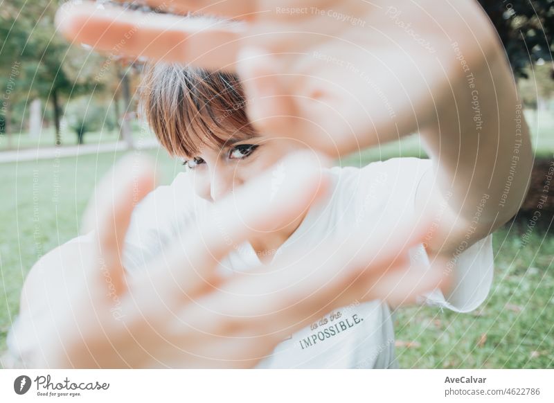 Junge Frau, die die Linse mit den Händen, während lächelnd zu Kamera schüchtern. Schüchternheit zu Kamera-Konzept, Angst, fotografiert Konzept. Jung und trendy, glücklich Spaß Witz.