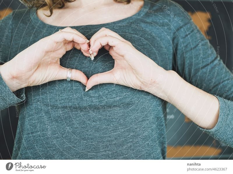 Junge Frau macht ein Herzzeichen mit ihren Händen Solidarität Menschlichkeit Hilfsbereitschaft Konzept konzeptionell Hand Truhe weiß wirklich Menschen