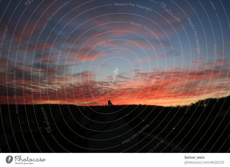 Ein Schornstein ragt aus dem dunklen Wohngebiet in den blutroten Himmel Sonnenuntergang Abenddämmerung Nacht Abendstimmung Wolken Häuser Dorf Wetter Stadt