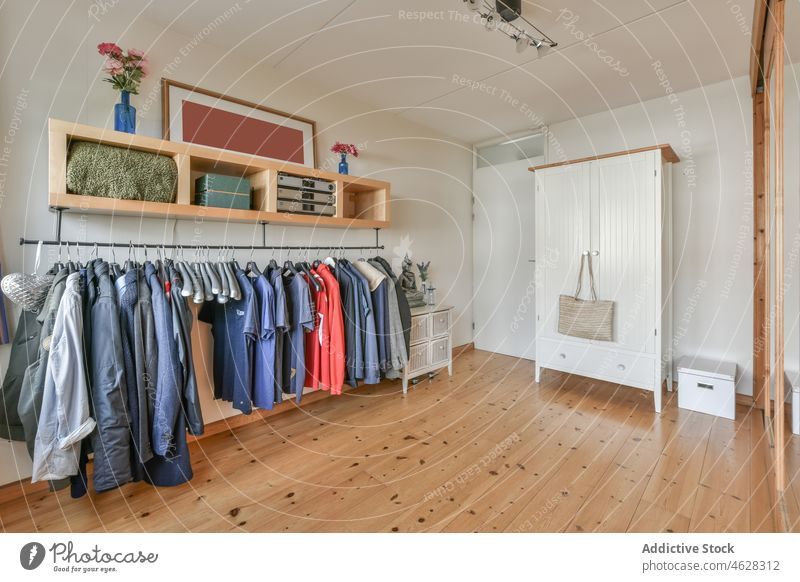 Interieur eines Umkleideraums mit hängenden Kleidern auf einem Gestell und Holzmöbeln Ankleidezimmer Kleiderschrank Kleidungsstück Ablage Kleiderbügel Schrank