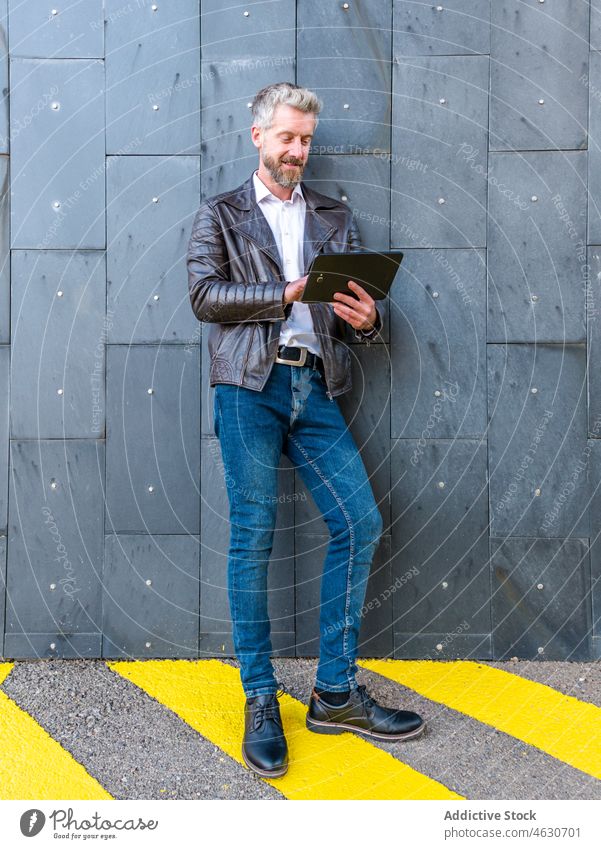 Trendiger Mann surft auf einem Tablet in der Nähe der Wand Tablette Straße Browsen online modern Großstadt Anschluss Talkrunde Internet männlich Vollbart Stil