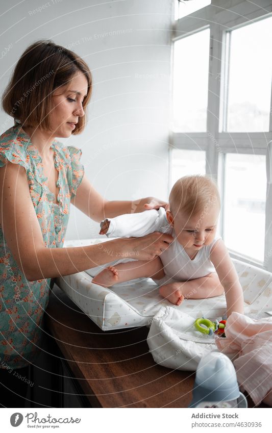 Mutter wickelt Baby am Fenster Kleid Stoff Mutterschaft Säuglingsalter Kinderbetreuung heimwärts heimisch mütterlich niedlich bezaubernd unschuldig Raum wenig