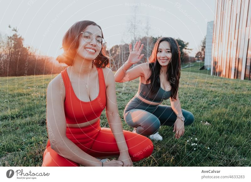 Zwei junge afrikanische Frauen, die sich während eines farbenfrohen Sonnenuntergangs im Gras hockend ausruhen, Porträt im Fokus. Training im Park nach der Arbeit, Workout in der Stadt, Spaß haben zusammen tun Übung