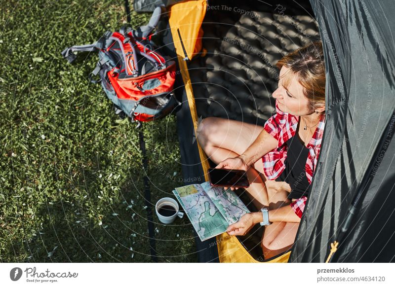 Frau plant nächste Reise, während sie mit Karte im Zelt sitzt. Frau entspannt im Zelt beim Camping im Sommerurlaub Urlaub Ausflug Abenteuer Campingplatz reisend