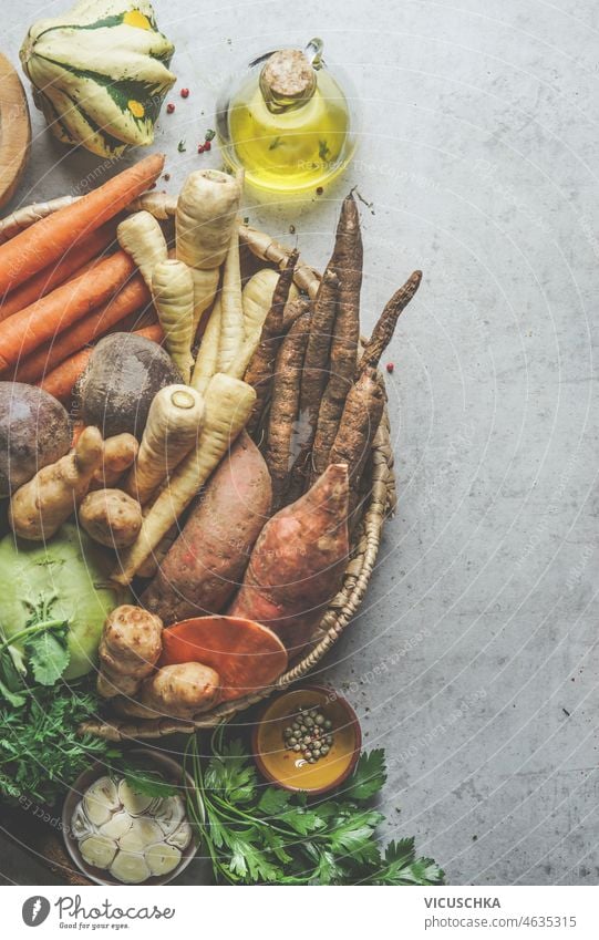 Lebensmittel Hintergrund mit Tablett mit verschiedenen Wurzelgemüse, Knoblauch und Gewürze auf grauem Beton Küchentisch. Pastinake, Süßkartoffel, Karotten, Kohlrabi und Rote Bete, Kochen mit saisonalen Zutaten. Ansicht von oben