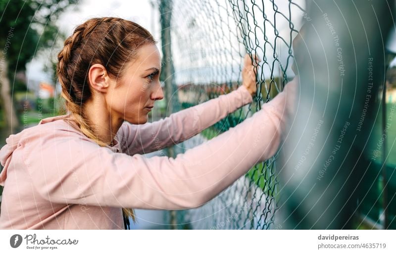 Seriöse Hafenarbeiterin mit Boxerzöpfen, die an einem Metallzaun lehnt ernst Frau Sportlerin Boxerflechten Lehnen Profil Frauenpower harte Frau Athlet