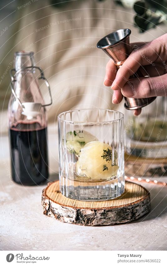 Sirup von Hand in einen Kräutercocktail mit Eiswürfeln gießen. organisch funkelnd Kräuterbuch aromatisch Glas Getränk Barmann Barkeeper Mixologe Mixologie