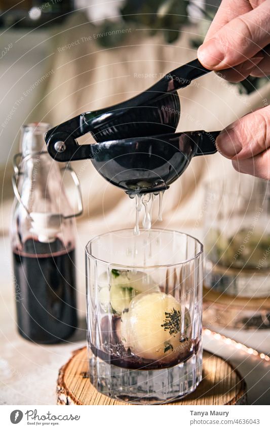 Auspressen einer Zitrone mit der Hand in einem Cocktail aus Edelbeersirup und Kräutereiswürfeln Glas Küche Rosmarin Schnaps selbstgemacht Lebensmittel