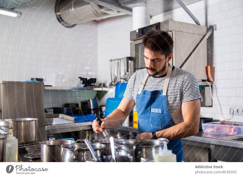 Junger ernsthafter ethnischer männlicher Koch, der Zutaten in einem Topf in der Küche umrührt Mann Speise rühren Konzentration kulinarisch Arbeit Restaurant