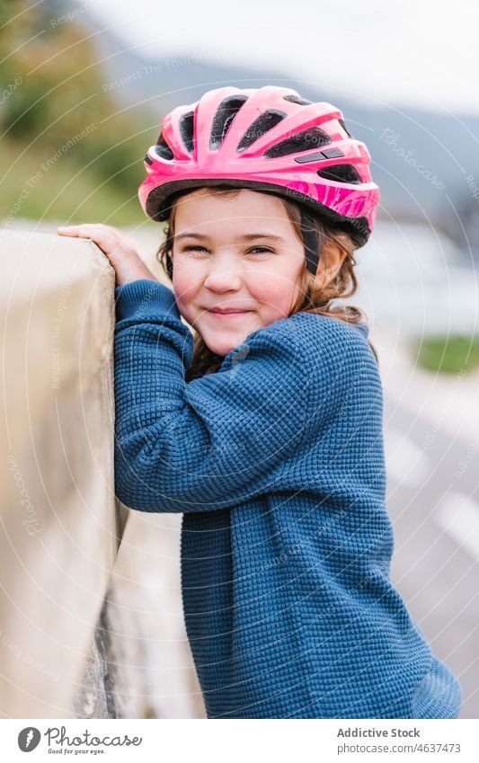 Mädchen mit Helm steht an der Grenze Kind Schutzhelm Hobby Lächeln Kindheit Straße Glück Freizeit Zeit verbringen froh Aktivität Borte Zaun Barriere Stein