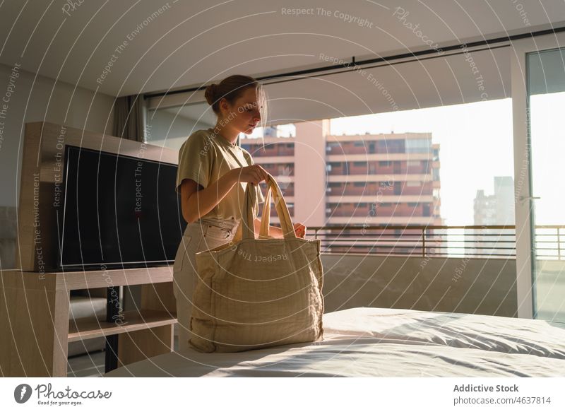 Junge Frau mit Tasche steht in der Nähe des Bettes in einem modernen Schlafzimmer Feiertag Hotel Urlaub Ausflug Windstille Tourist Unterkunft reisen jung lässig