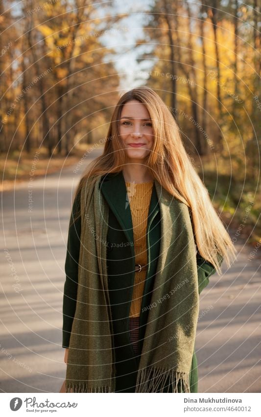 Schöne Frau in grünem Mantel und gelben Pullover im Herbst Park in der Nähe von Bäumen mit gelben Blättern bei Sonnenuntergang. Verbringen Sie Zeit in der Natur, um Frieden im Kopf, entspannende Momente und minfullness zu halten. Herbst-Stil und Mode, lässige Kleidung.