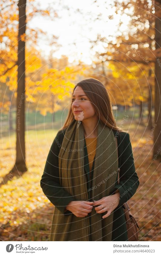 Schöne Frau in grünem Mantel und gelben Pullover im Herbst Park in der Nähe von Bäumen mit gelben Blättern bei Sonnenuntergang. Verbringen Sie Zeit in der Natur, um Frieden im Kopf, entspannende Momente und minfullness zu halten. Herbst-Stil und Mode, lässige Kleidung.