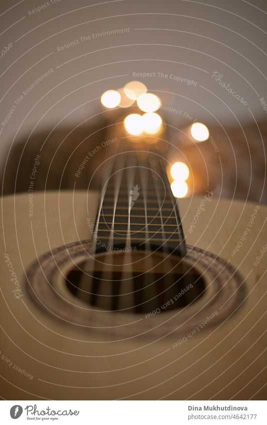 Gitarre mit gemütlichen Lichtern Bokeh Nahaufnahme. Person spielt akustische Gitarre zu Hause mit Weihnachtsbeleuchtung - Hand auf Saiten Nahaufnahme.