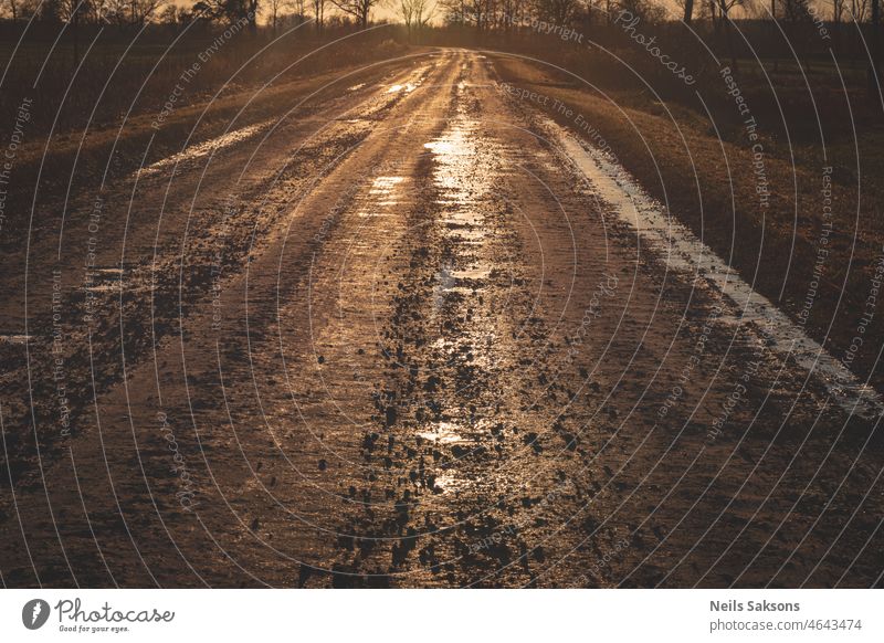 schmutziger Sand und Schotterstraße mit Pfützen im goldenen Licht des Sonnenuntergangs abstrakt Hintergrund blau braun Ton Nahaufnahme Cloud Land Landschaft Tag