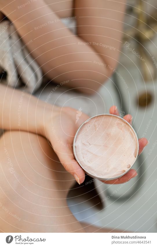 Frau trägt Feuchtigkeitscreme oder -lotion auf die Haut auf, Nahaufnahme. Ein Tiegel mit einer Hautpflegecreme in einem Badezimmer. Kosmetik Produkt medizinisch