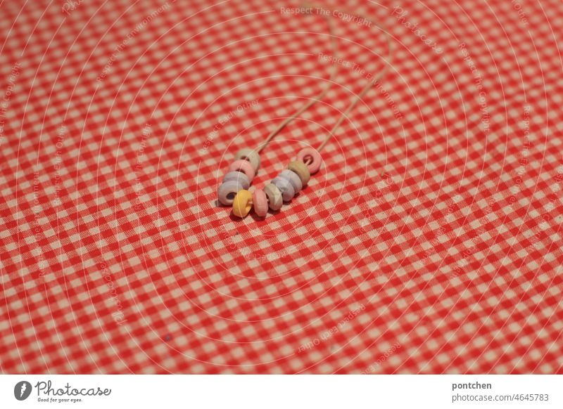 eine zuckerperlenkette liegt auf einem tisch mit rot-weiß karierter tischdecke. nostalgie. nostalgische süßigkeiten kindheit ungesund kalorien Lebensmittel