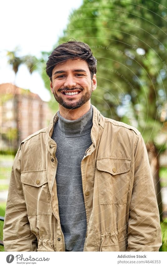 Lächelnder bärtiger Mann in Jacke im Park stehend positiv Porträt Persönlichkeit cool Individualität Vorschein Blick Glück männlich Inhalt froh Optimist