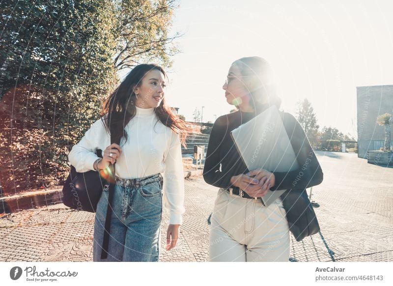 Zwei junge Studentinnen, die zum Unterricht gehen, während sie an einem hellen Tag im Freien mit der Fakultät sprechen und lachen. Universität Studien, College Papiere, modernen Stil. Die Vorbereitung einer Präsentation für die Klasse.