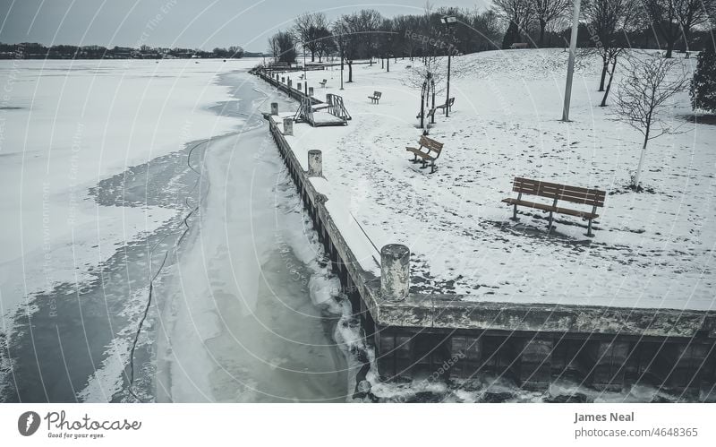 Die Uferlinie, die den Park entlangführt, ist gefroren. Schnee bedeckt das Land mit Bäumen und Bänken. Horizont Oberfläche Farbe Seeufer Natur Wasser eisig