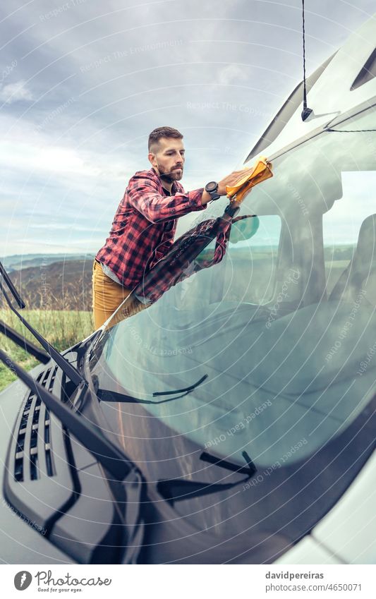 Mann beim Reinigen der Windschutzscheibe eines Wohnmobils im Freien jung Trocknung Spülung Kleintransporter Glas Stoff vorsichtig Besitzer Perfektionist reiben