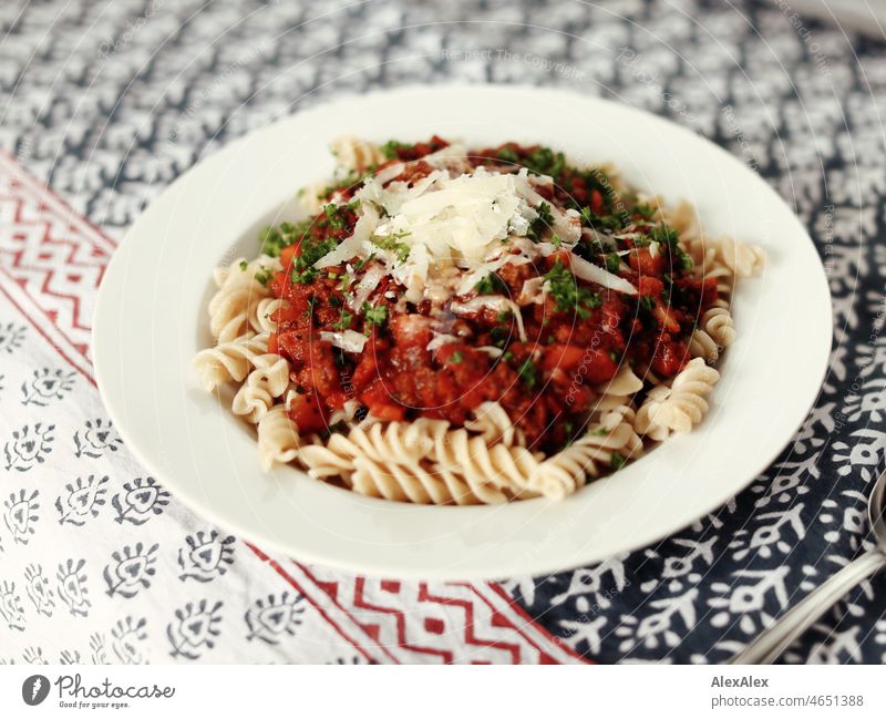 Suppenteller mit Spirelli/Fusilli und Sauce Bolognese mit Parmesankäse und frischem Basilikum Tischdecke Muster Teller Besteck Löffel Porzellan Pasta