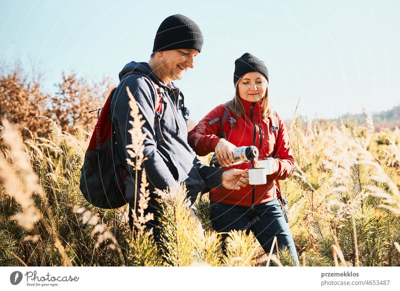 Paar entspannt und genießt den Kaffee während der Urlaubsreise. Menschen stehen auf dem Weg gießen Kaffee aus Thermoskanne. Paar mit Rucksäcken Wandern durch hohes Gras entlang Weg in den Bergen. Aktive Freizeit in der Nähe der Natur