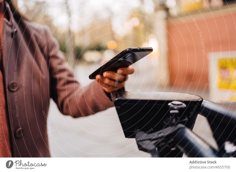 Crop-Frau, die einen E-Scooter mit Mobiltelefon mietet Klient Smartphone Funktelefon Miete App Anwendung Scan Telefon e-Scooter elektrisch Straße Großstadt