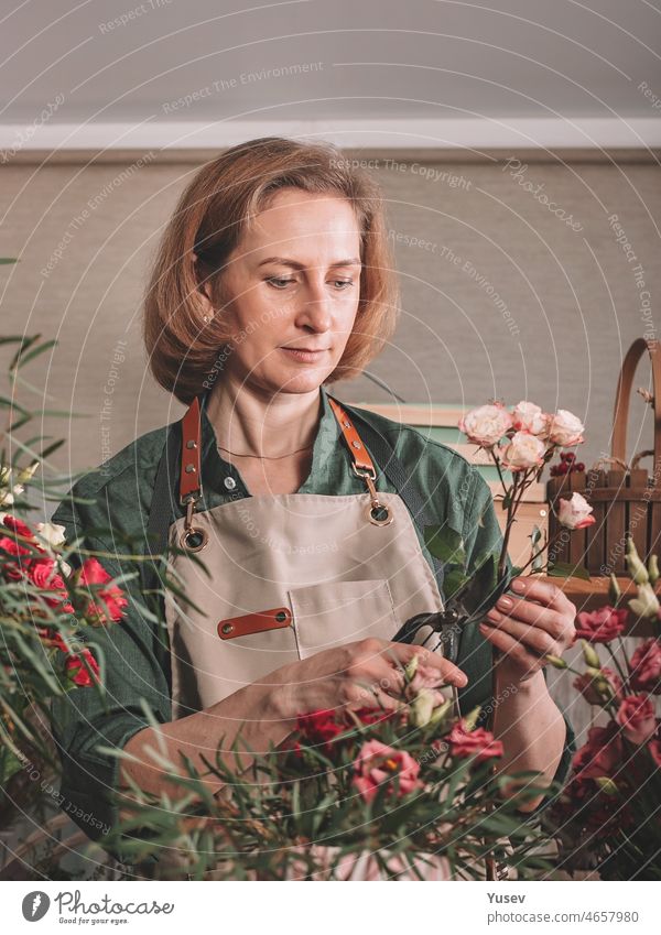 Schöne Frau Florist macht ein Geschenk Strauß Rosen. Florist Arbeitsplatz. Kleines Geschäftskonzept. Frontansicht. Blumen und Zubehör. schön Blumenhändler